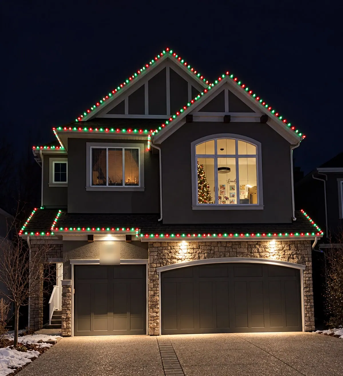 Two-storey home with alternating red and green bulbs along every gable and roofline above a double garage at night