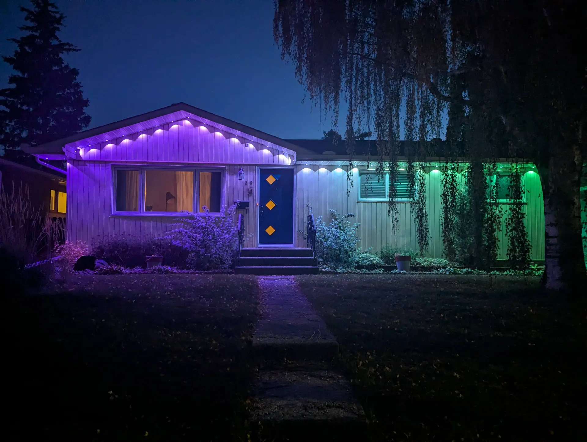 Govee permanent lights mounted under the eaves of a bungalow, shining down onto the walls in purple and green at dusk